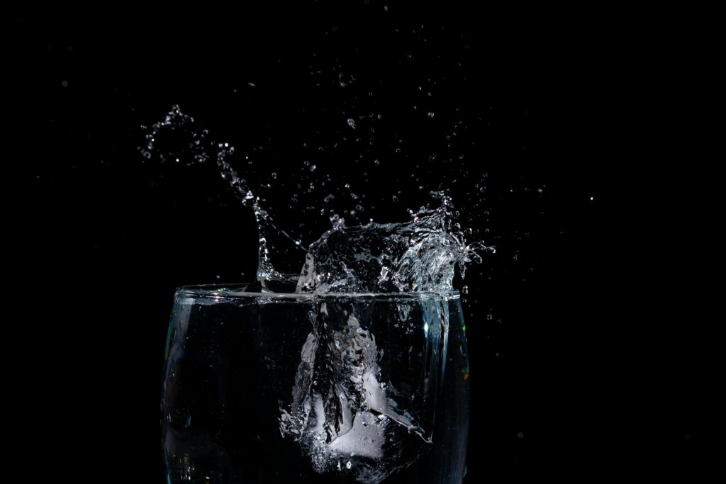High-speed capture of water splashing out of a glass against a black backdrop, showcasing liquid motion.
